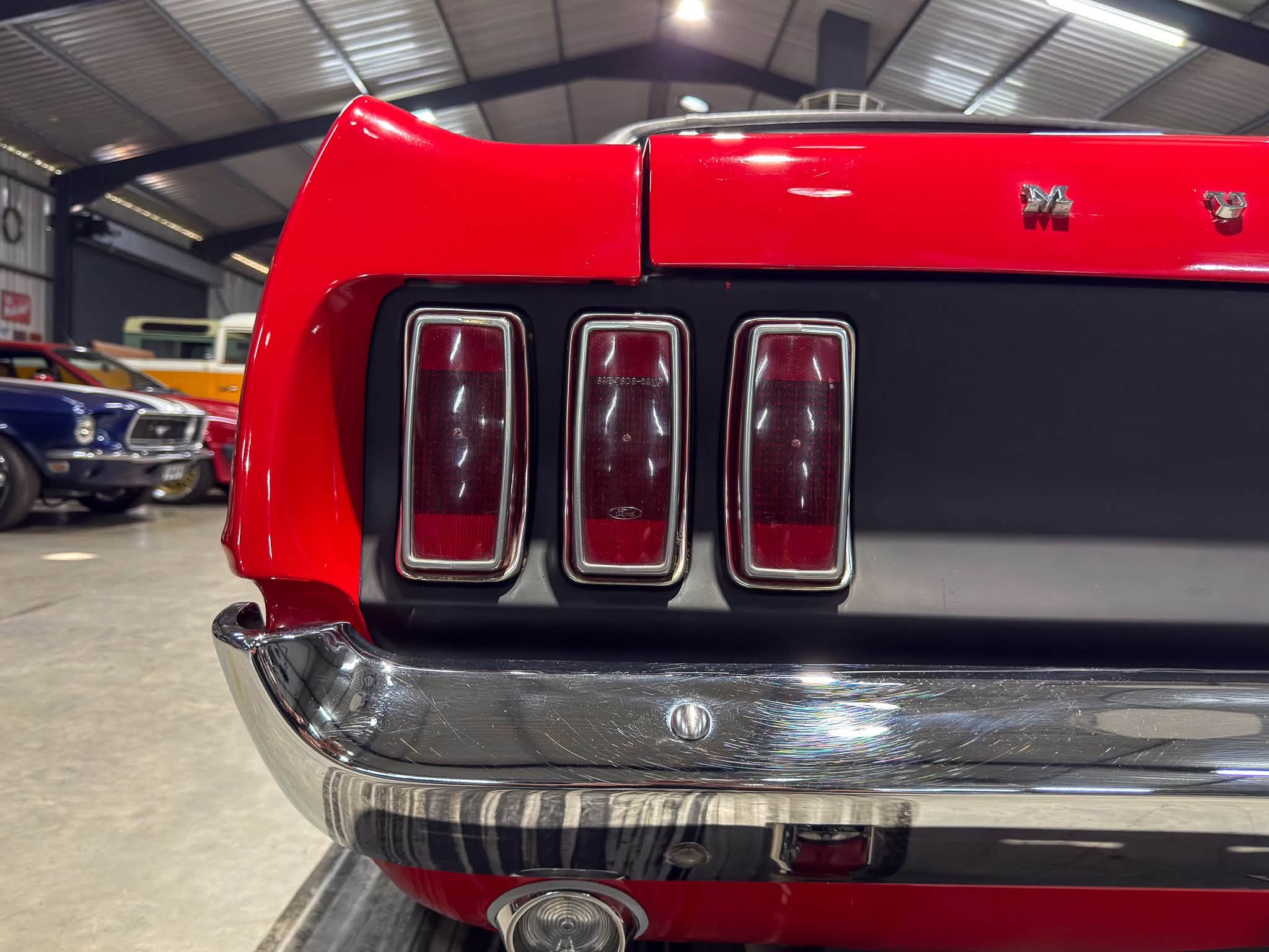 Rear end of a red vintage car with three vertical tail lights and chrome bumper inside a showroom.