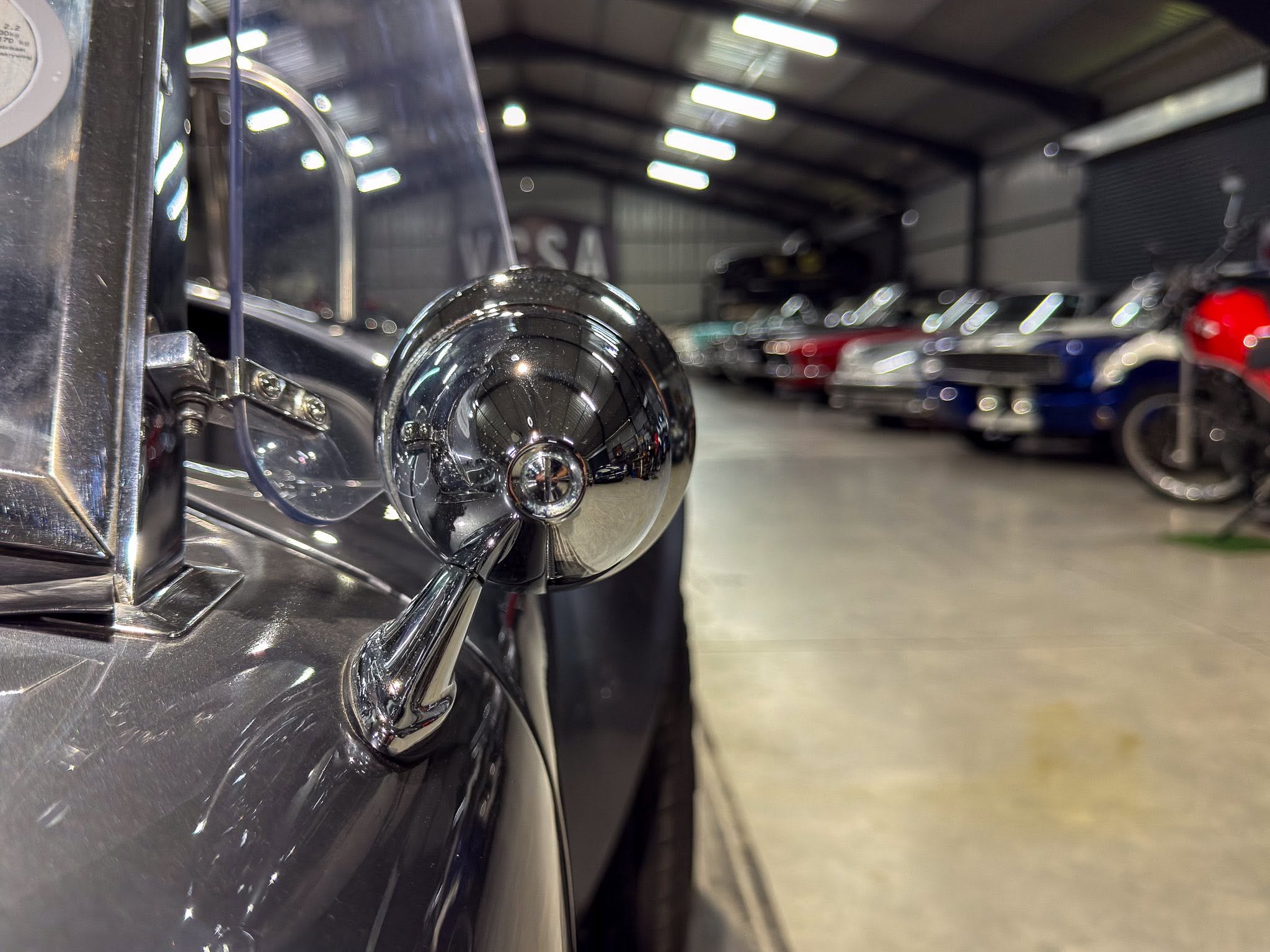 Close-up of a shiny black car headlight on a dark vehicle in an indoor garage or showroom.
