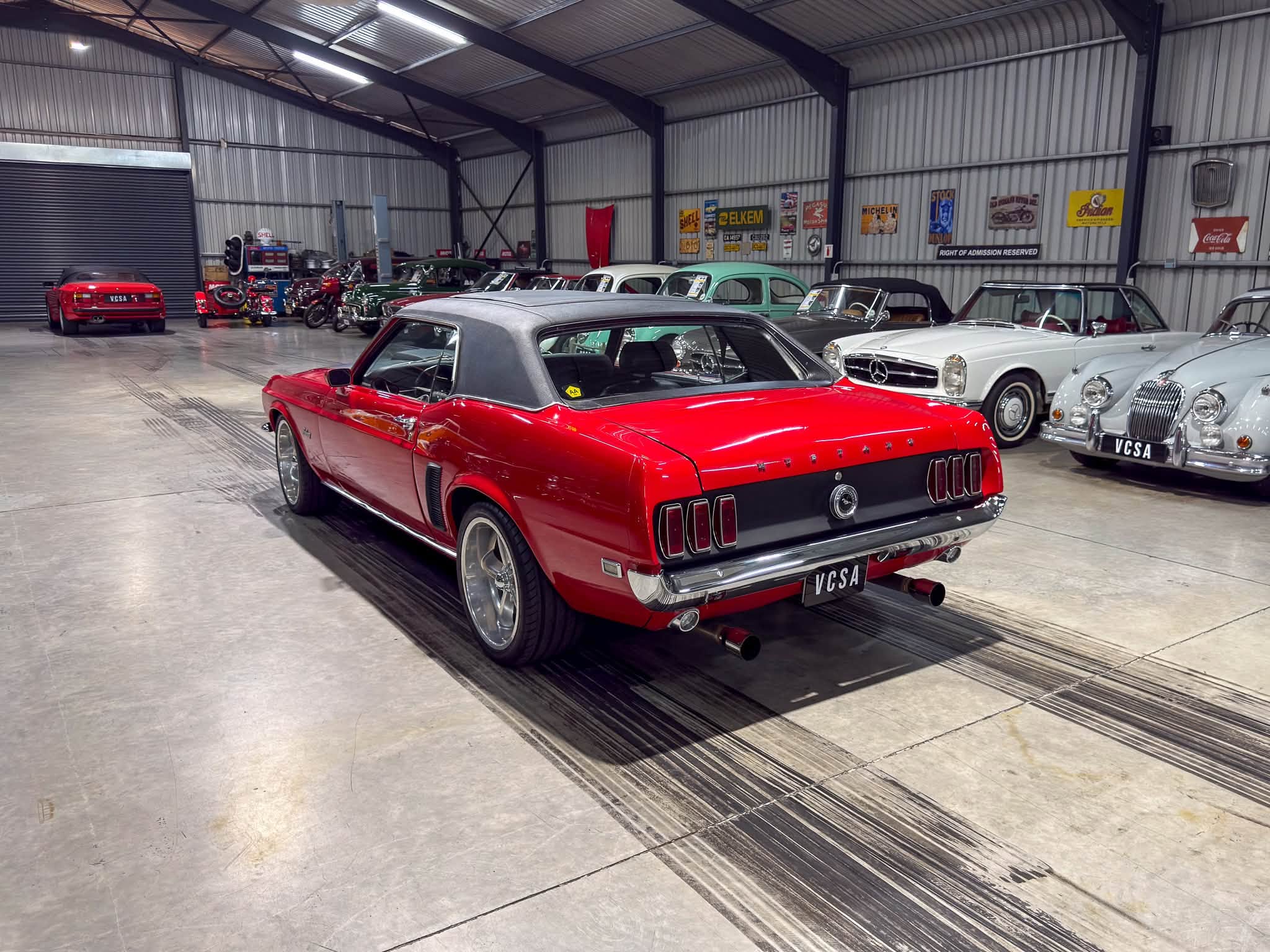 Interior of a vintage car showroom with a red convertible in the foreground and classic cars along the wall
