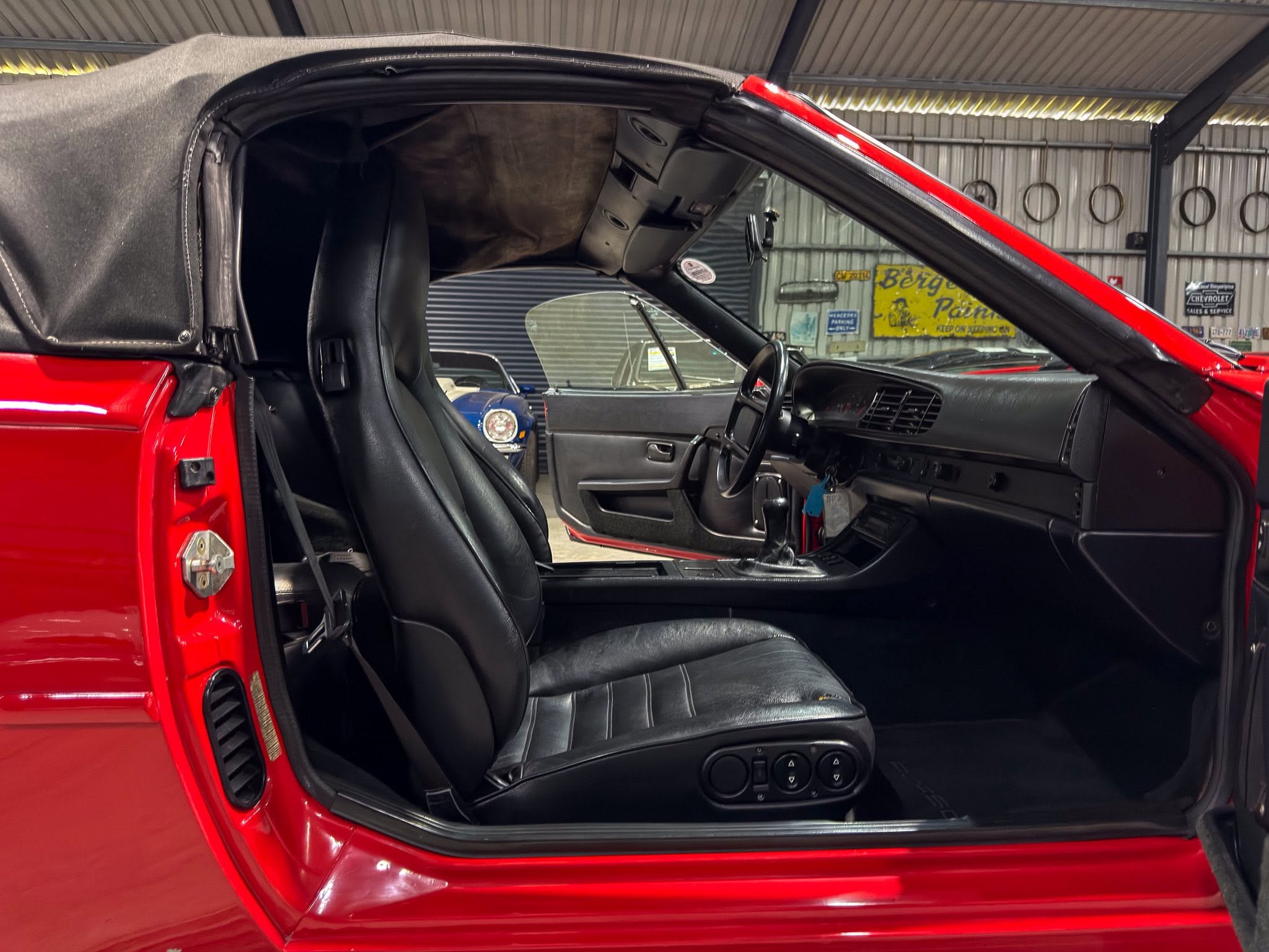 Red convertible car interior with black leather seats and the top down inside a garage or showroom garage space.