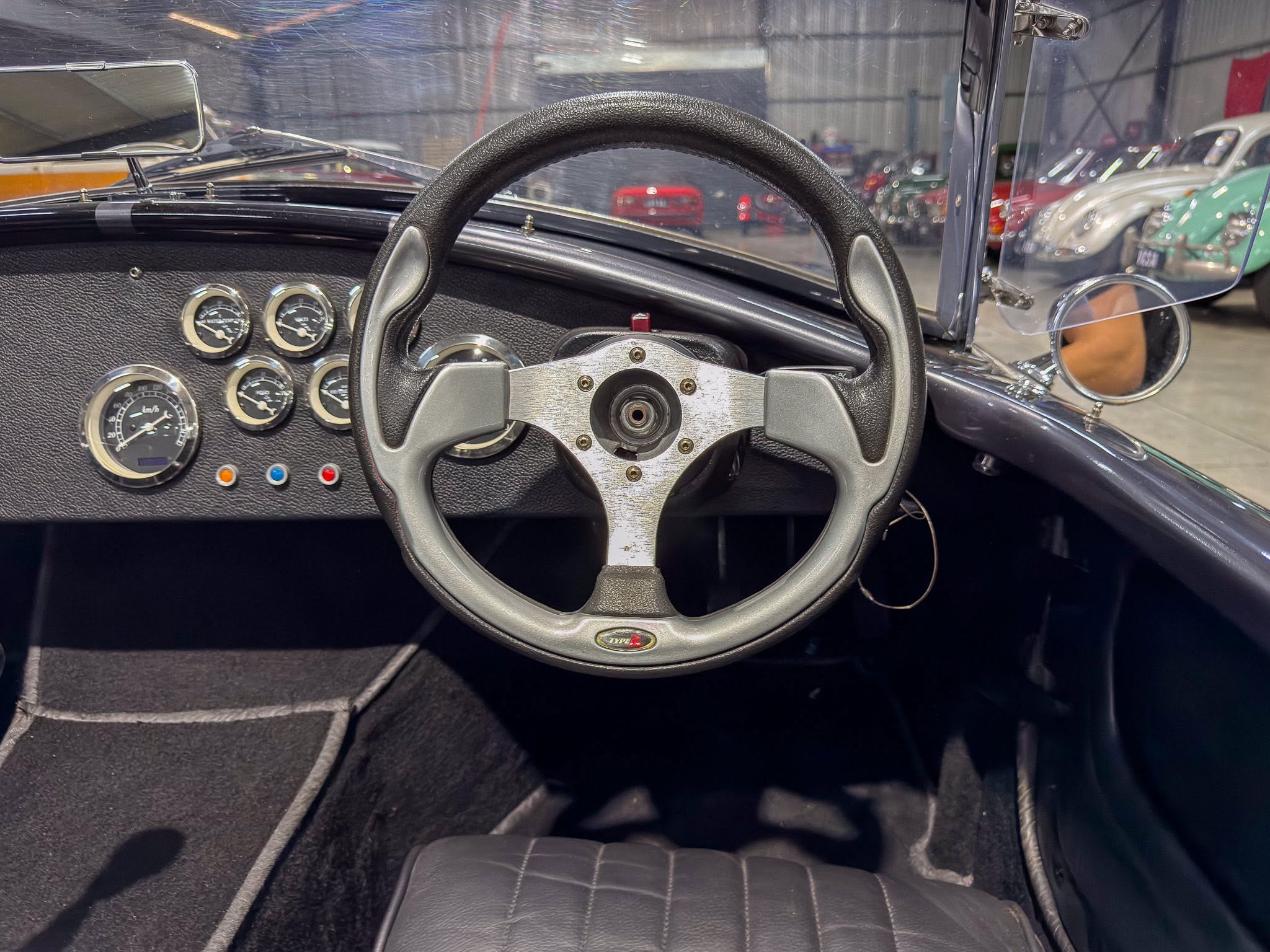 Interior of a vintage car: steering wheel and classic gauge cluster on a textured black dashboard, chrome accents visible.",