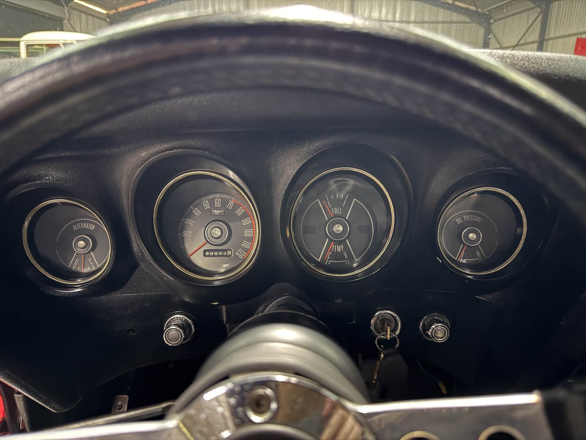 View of a car dashboard from the driver’s perspective, showing speedometer, fuel gauge, and other gauges with a steering wheel in front.