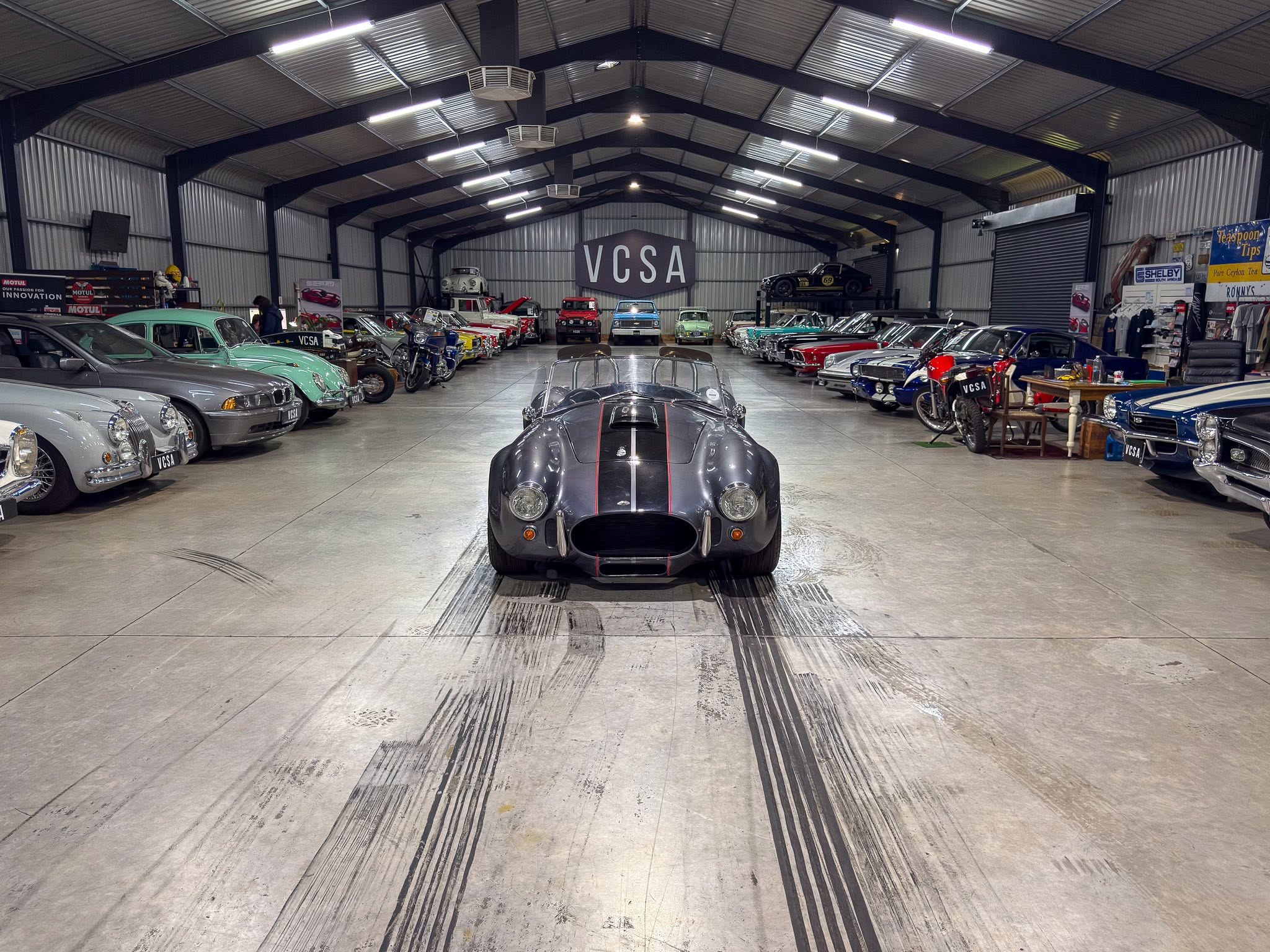 Gray vintage racecar in a large showroom, rows of classic cars on both sides and a VCSA banner in the back.