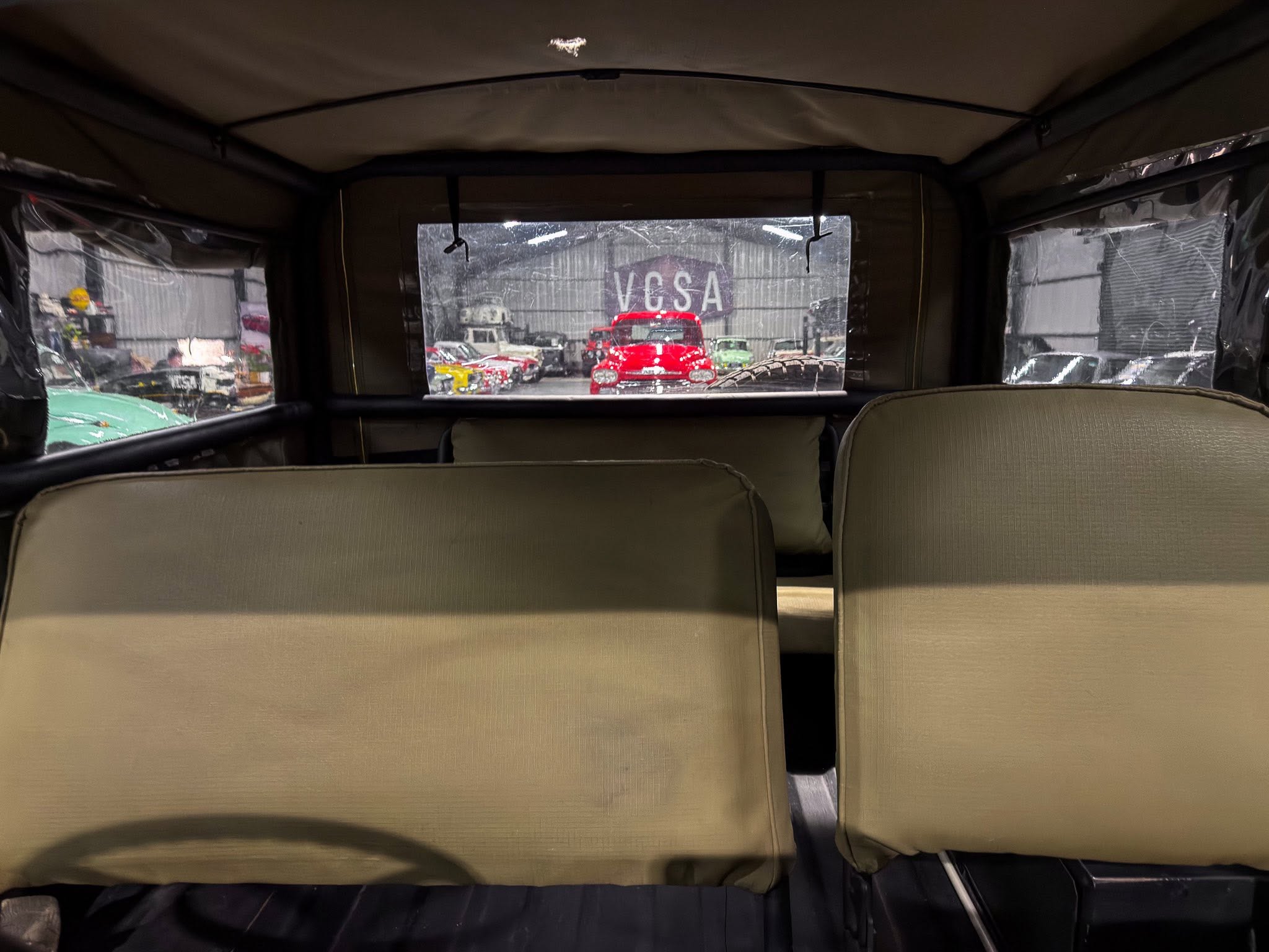 Interior of a vintage car showing beige seats and rear window view to a row of classic cars in a showroom outside the vehicle.