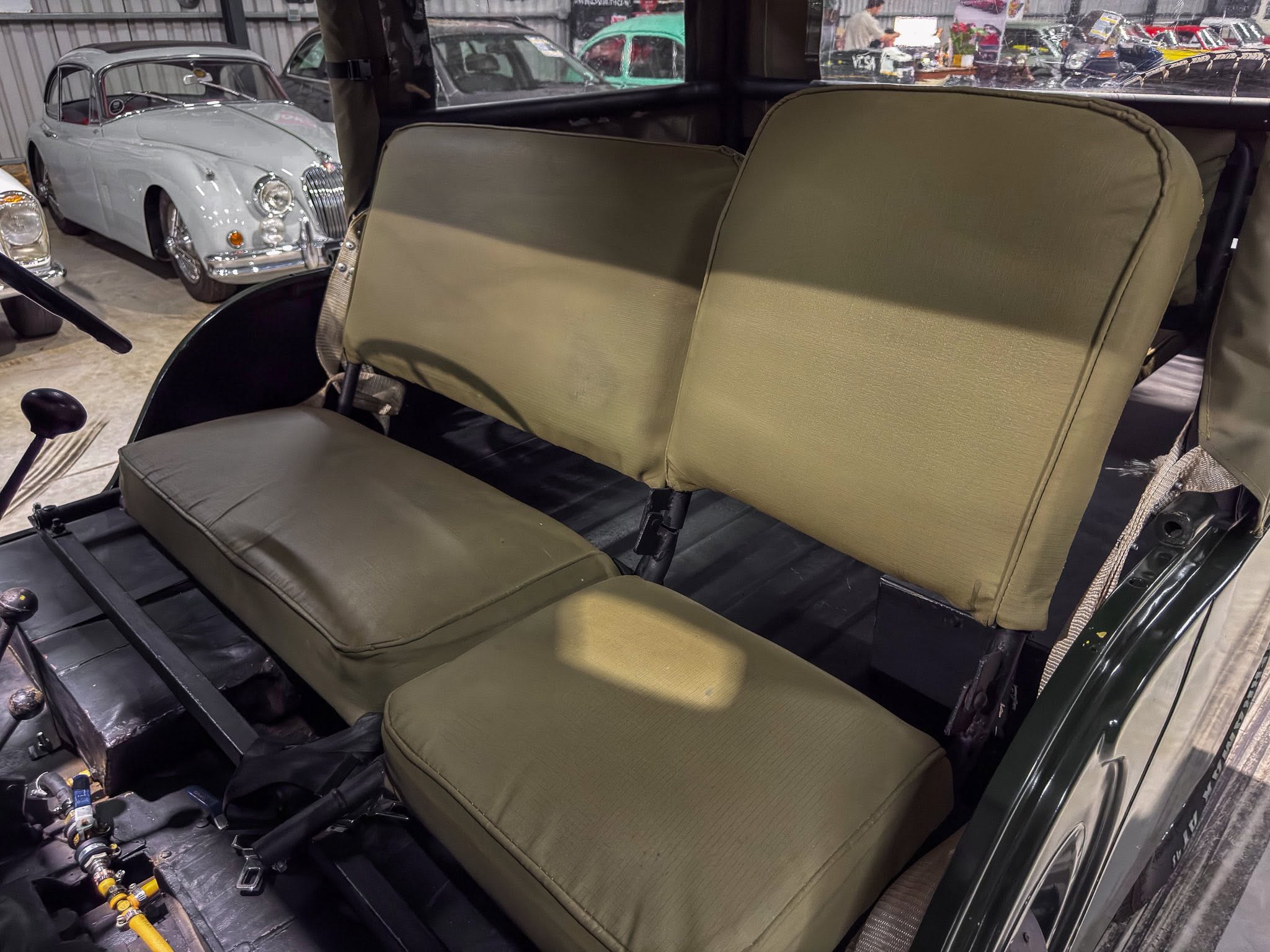 Olive-green vintage car interior with bench seats; classic cars on display visible through the windows.