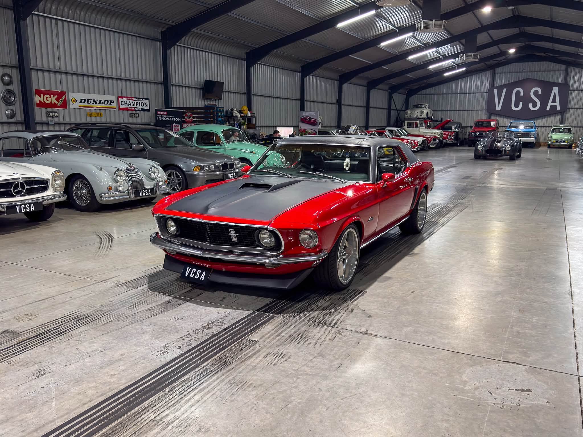Interior of a spacious showroom filled with vintage cars, the red convertible in the foreground and many classic vehicles in the background.