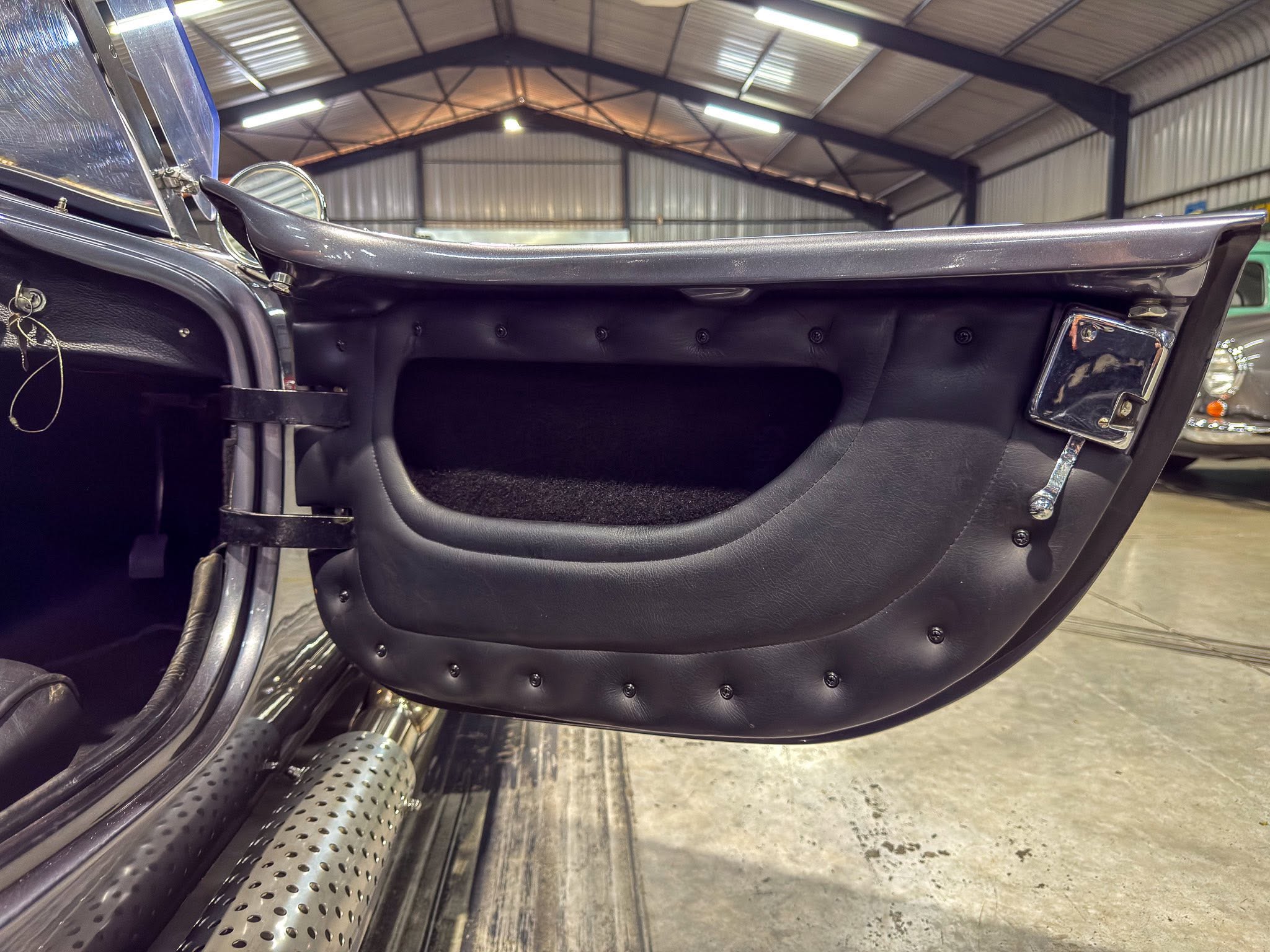 Open vintage car door showing black leather interior and chrome hardware inside a workshop garage