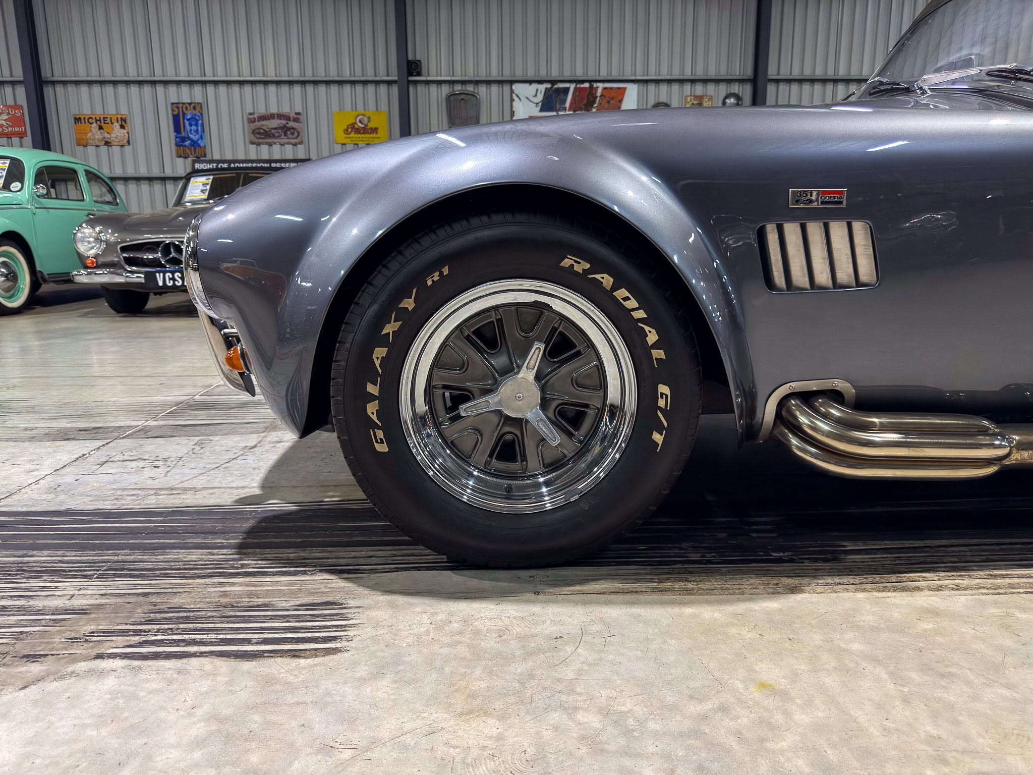 Close-up of a vintage car wheel and front fender in a showroom with other classic cars in the background