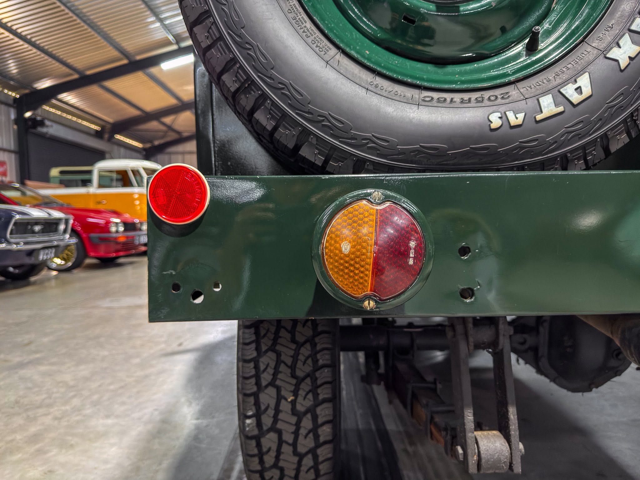 Rear view of a green vintage truck with a mounted spare tire, taillight, and visible wheel in a showroom setting.