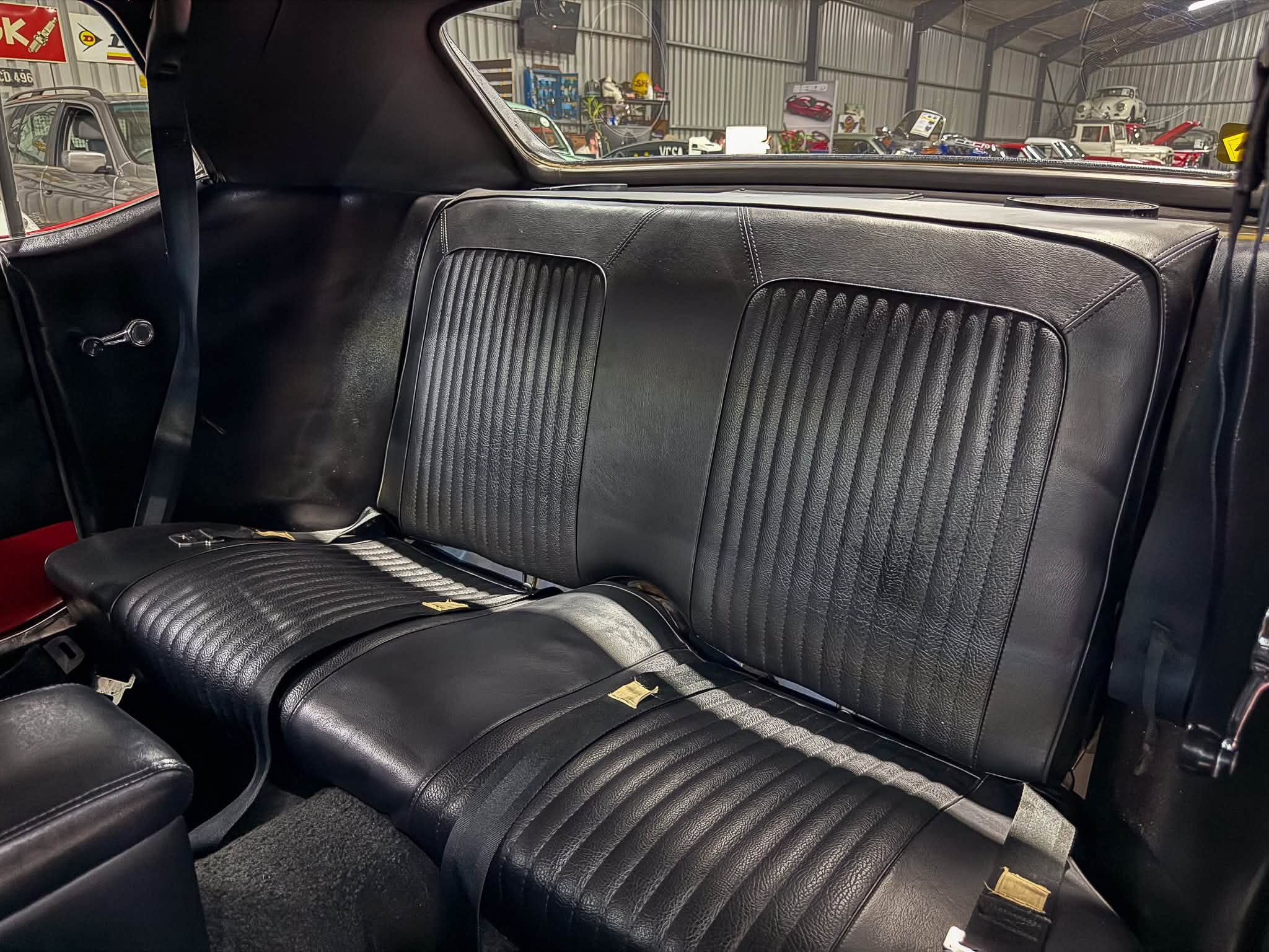 Black leather back seats with vertical stitching and scattered tan debris inside a car interior. Seen showroom cars through rear window.
