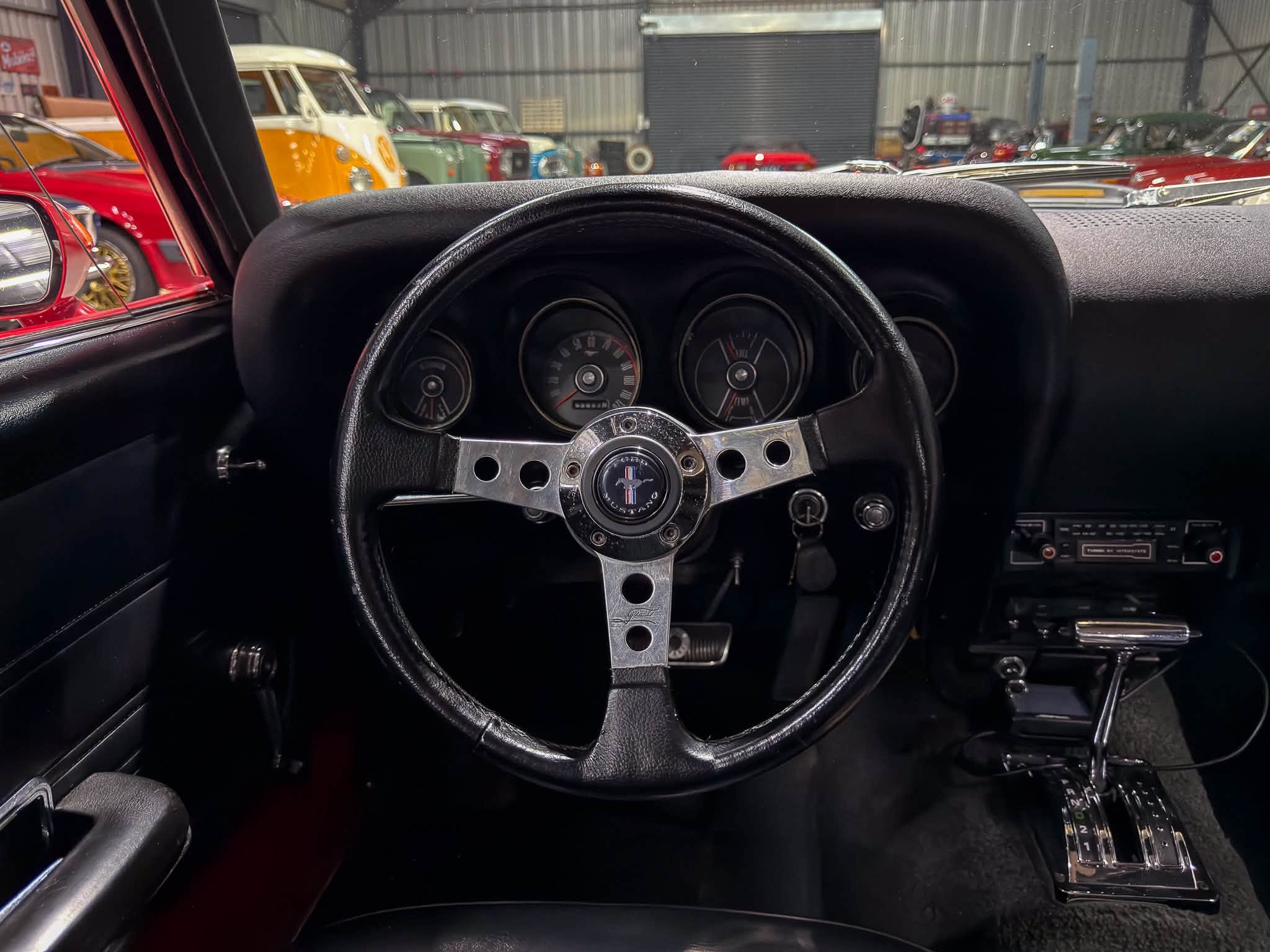 Steering wheel and vintage dashboard of a classic car with a row of retro vehicles visible through the windshield in a showroom.