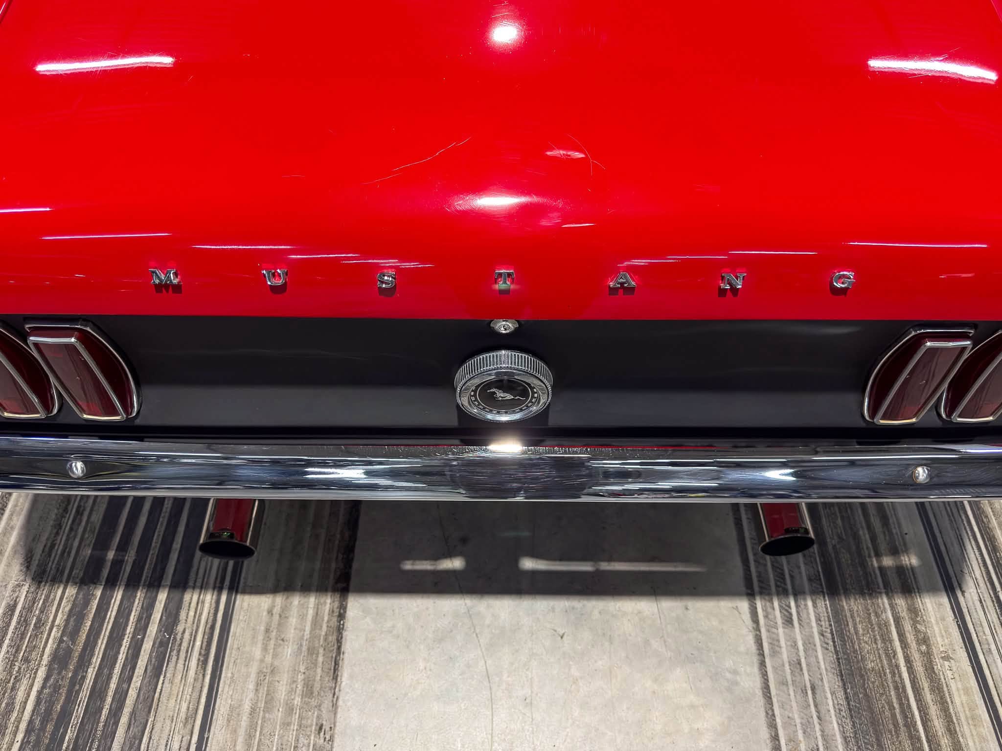 Rear view of a red Ford Mustang showing chrome MUSTANG lettering across the trunk and a circular emblem between two taillights on a chrome bumper.