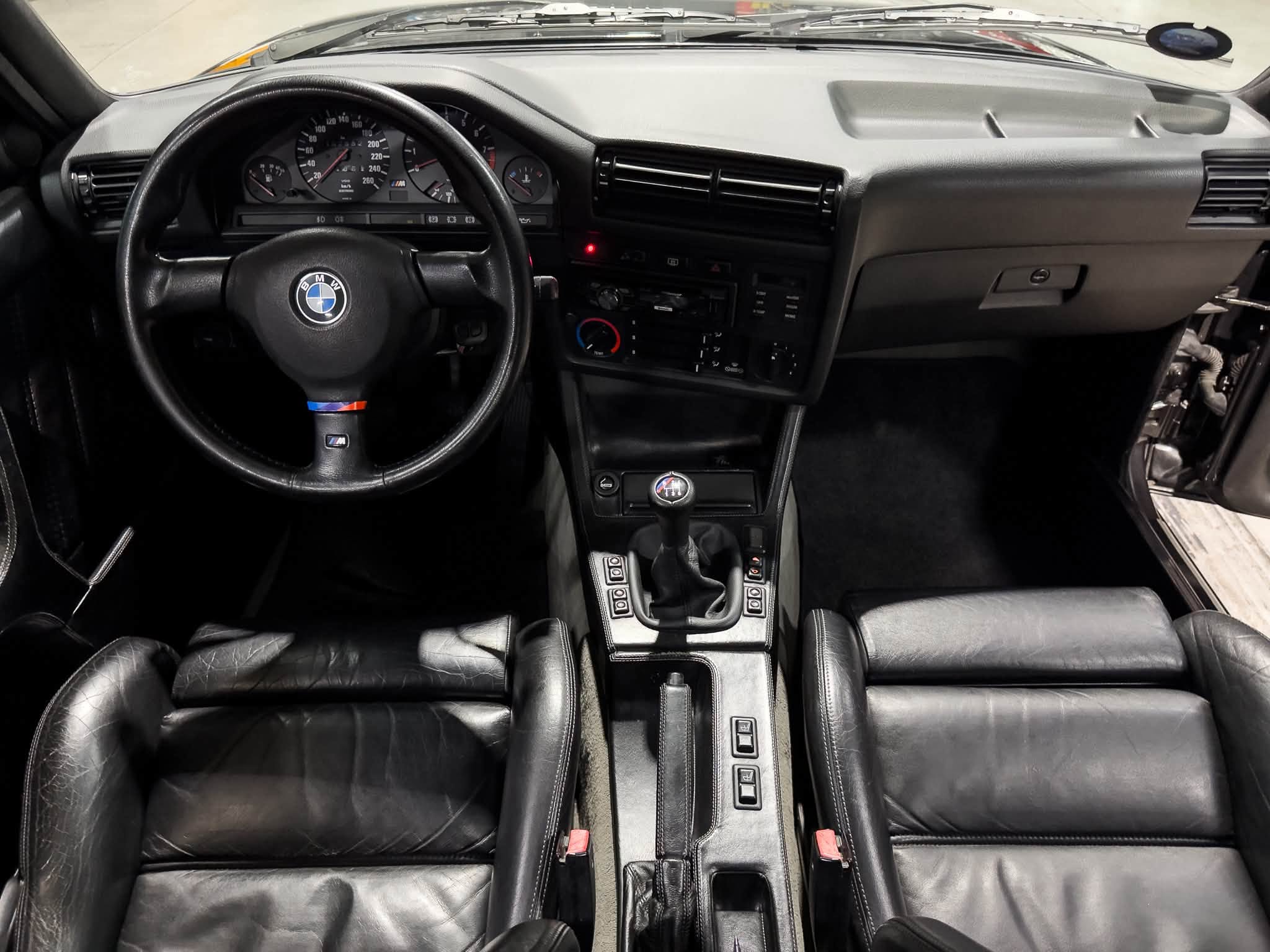 Driver's seat view of a black BMW interior with leather seats, steering wheel, and center console.