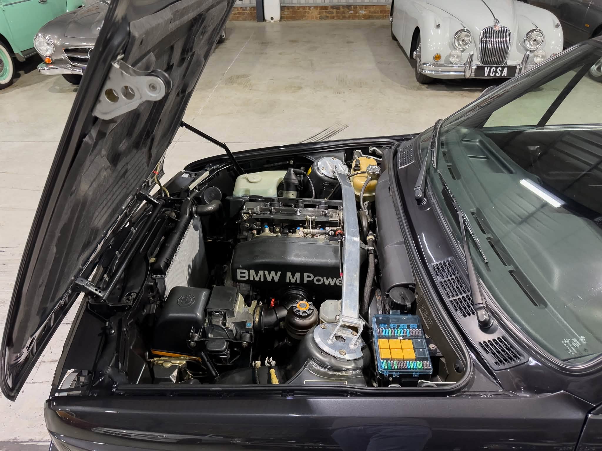 Open car hood revealing a BMW engine bay with 'BMW M Power' branding and various components surrounding the engine.