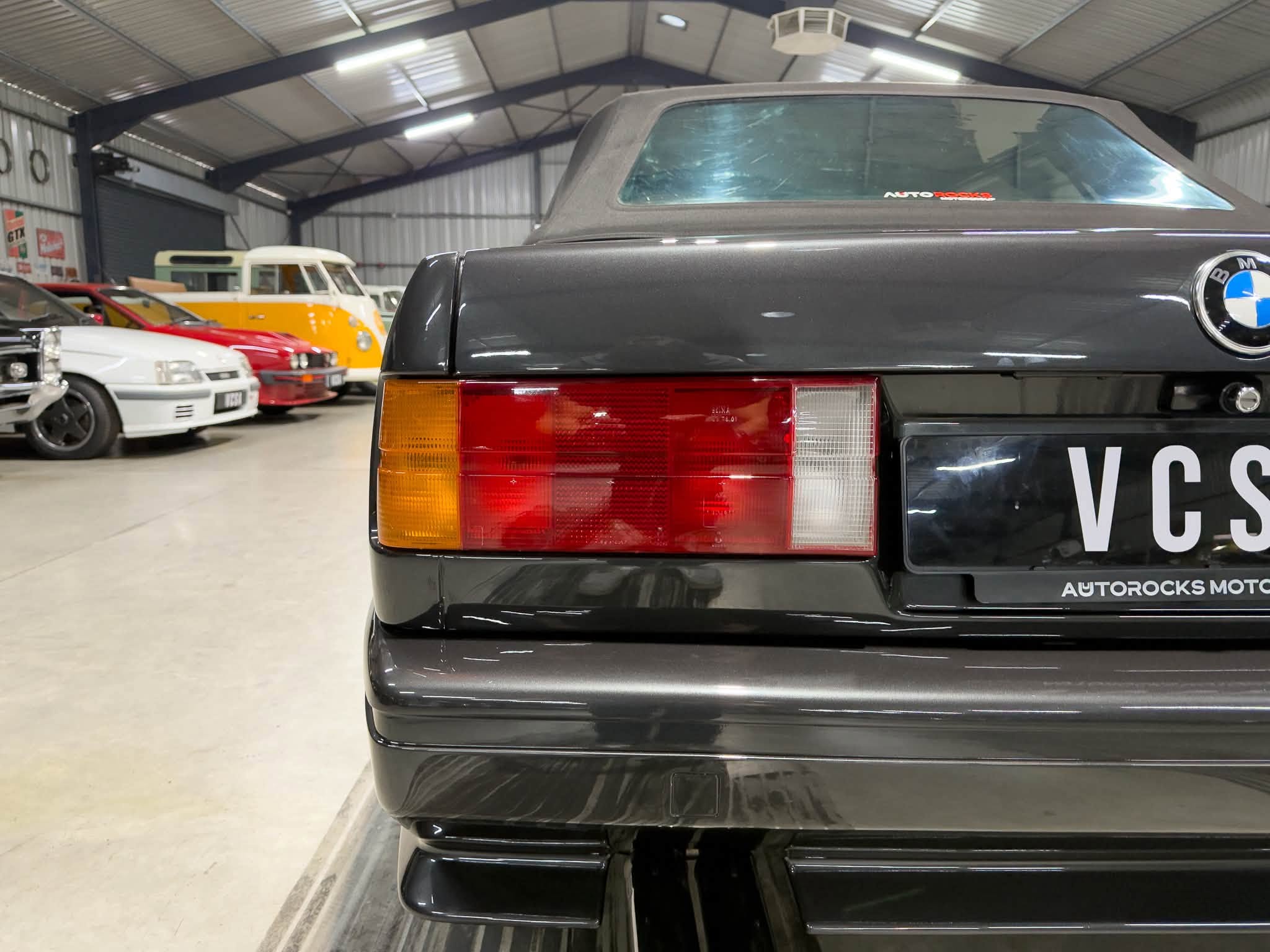 Rear of a black BMW classic car in a warehouse-style showroom with other vintage vehicles in the background.